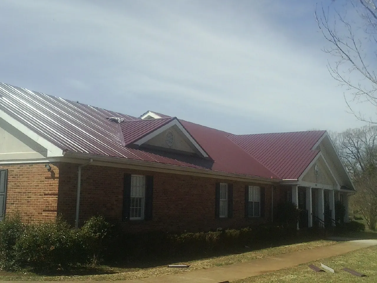 Red metal roof with gabled entries on a long brick building, from a Hail Damage Roof Repair job in Comstock