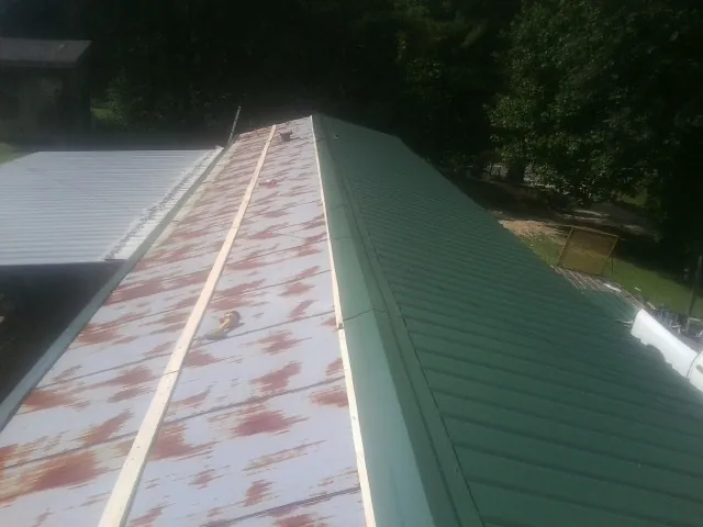 Old rusted panels beside newly installed green metal roofing — Wind Damage Roof Repair by Roofing Brothers in Comstock