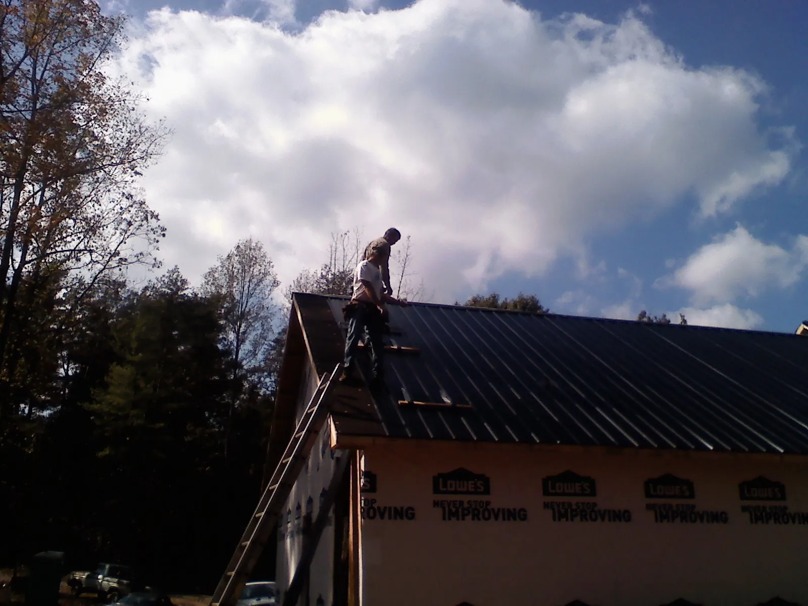 Roofer fastening dark metal panels high against a cloudy sky, from a Roof Inspection job in Comstock
