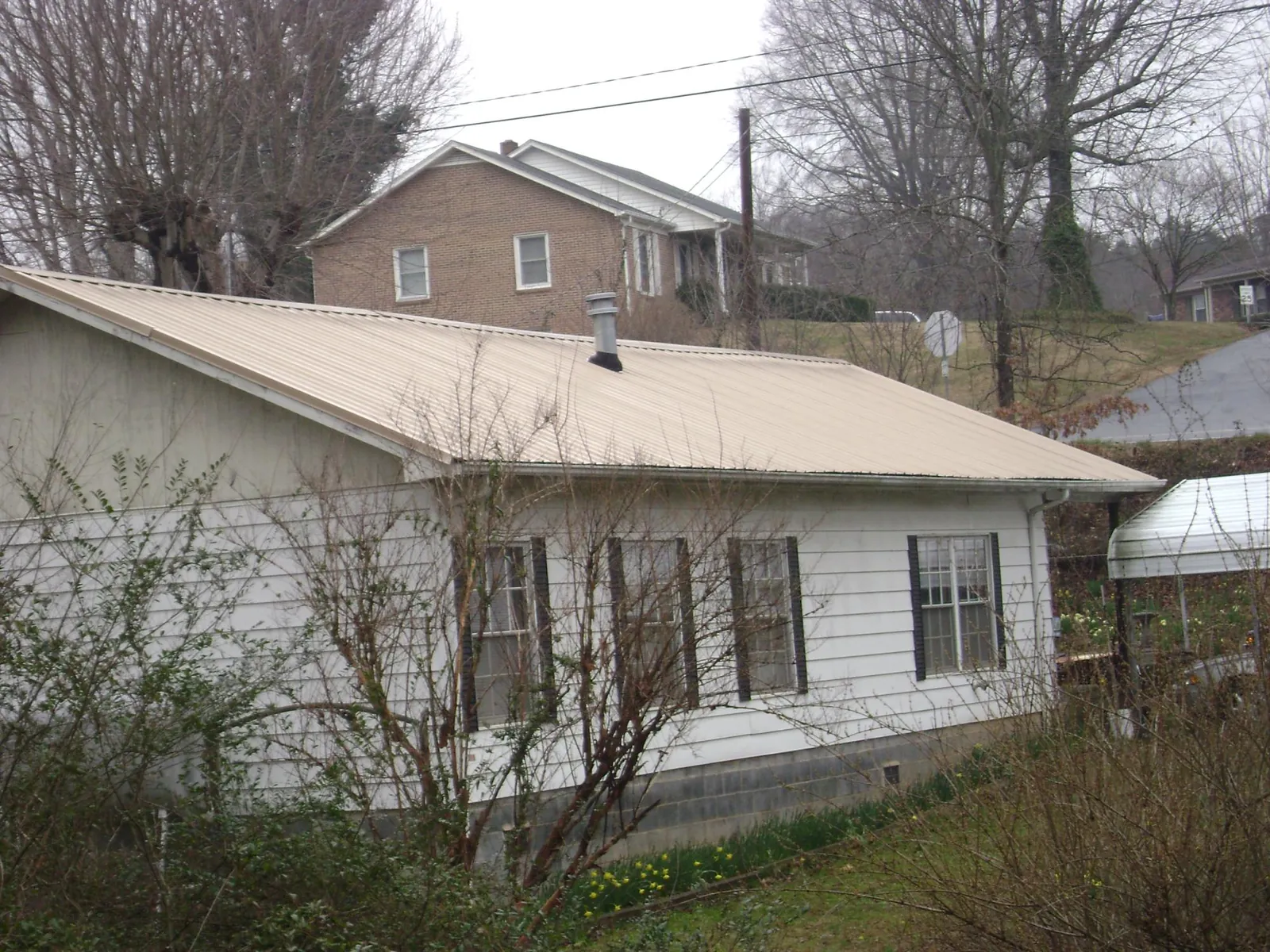 Tan metal roof on a white sided house set into a hillside — Commercial Roofing by Roofing Brothers in Comstock