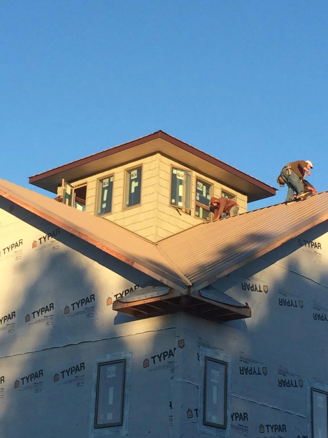 Roofers working around a rooftop cupola on a new metal roof at sunset — Roof Waterproofing in Comstock by Roofing Brothers